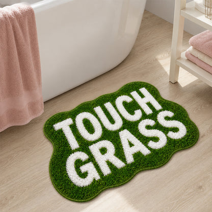 Green TOUCH GRASS bath mat on wood floor in front of a bathtub
