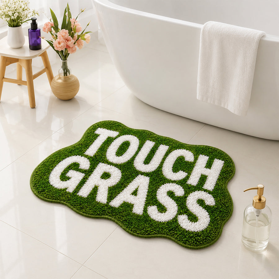 Feblilac TOUCH GRASS funny bath mat next to a bathtub with fresh flowers
